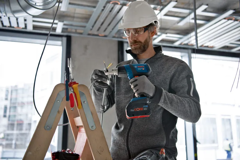 GHG 18V-50 A person wearing safety equipment uses a cordless heat gun on electrical wiring.