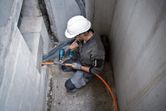 A person wearing safety equipment uses a cordless heat gun to work on an orange cable.