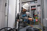 A person wearing safety equipment uses a cordless heat gun on electrical wiring.