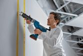 Person wearing safety equipment applies sealant to a wall with a cordless caulking gun.