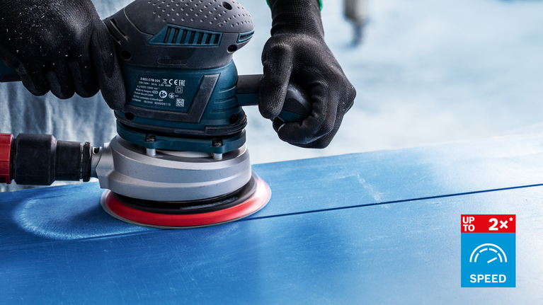 Person wearing safety equipment sands a blue surface with a power sander.