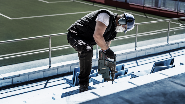 EXPERT SDS plus-7X Hammer Drill Bit Set 5/6/6/8/8/10/12 mm 7-pc A person wearing safety equipment drills into a concrete stadium step.