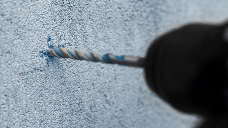 EXPERT HEX-9 MultiConstruction Drill Bit Set 5/6/8 mm 3-pc Drill creating a hole in a textured concrete wall.