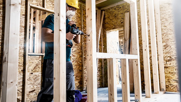 EXPERT Self Cut Speed Spade Drill Bit Set 20/22/25 mm 3-pc A person wearing safety equipment drills into a wooden frame at a construction site.