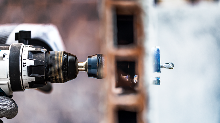 EXPERT Power Change Plus Hole Saw System Arbor 11 mm, HSS-G Drill 7.15 x 105 mm, 2-pc A person wearing safety equipment drills through a brick wall.