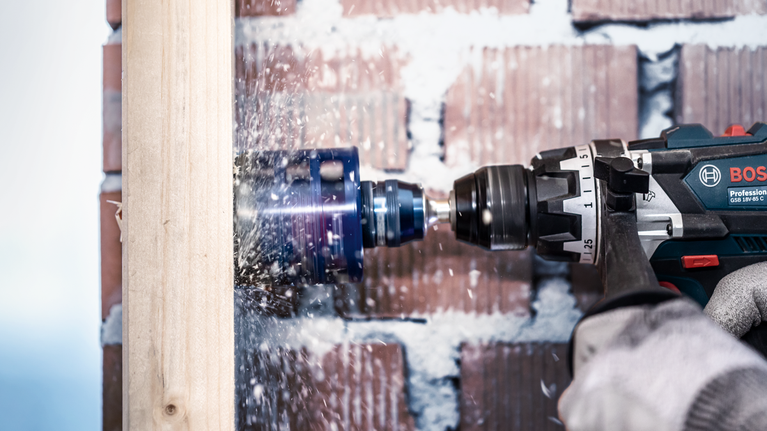 EXPERT Power Change Plus Hole Saw System Arbor 11 mm, HSS-G Drill 7.15 x 105 mm, 2-pc Person wearing safety equipment drills a large hole in a wooden beam.