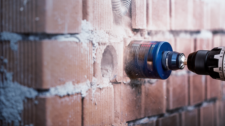 EXPERT Power Change Plus Hole Saw System Arbor 11 mm, HSS-G Drill 7.15 x 105 mm, 2-pc Hole saw attachment drilling a circular opening in a brick wall.