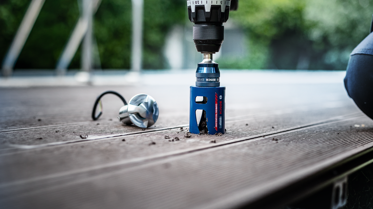 EXPERT Construction Material Hole Saw Set 20/25/32/38/51/64 mm 10-pc Power tool drilling a precise hole in a wooden plank outdoors.