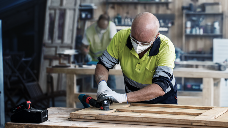 EXPERT Sanding Plate AVZ 90 RT10 Multitool Blade 90 mm A person wearing safety equipment sands a wooden frame with a power tool.
