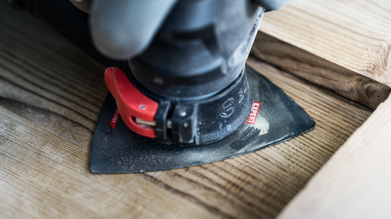 EXPERT Sanding Plate AVZ 90 RT10 Multitool Blade 90 mm A person uses a power tool with a sanding attachment to smooth wooden boards.