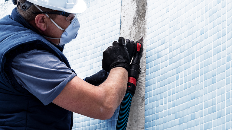 EXPERT Sanding Plate AVZ 90 RT2 Multitool Blade 90 mm A person wearing safety equipment grinds concrete next to blue tiles.