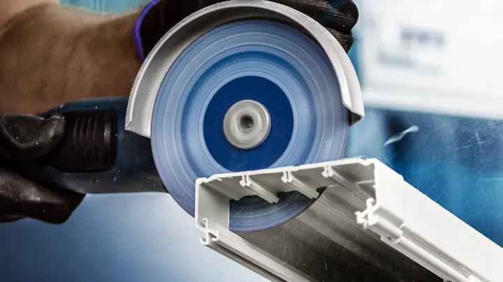 Person wearing safety equipment cuts a metal channel with an angle grinder.
