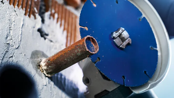 A metal pipe is being cut through a wall using a circular power saw blade.