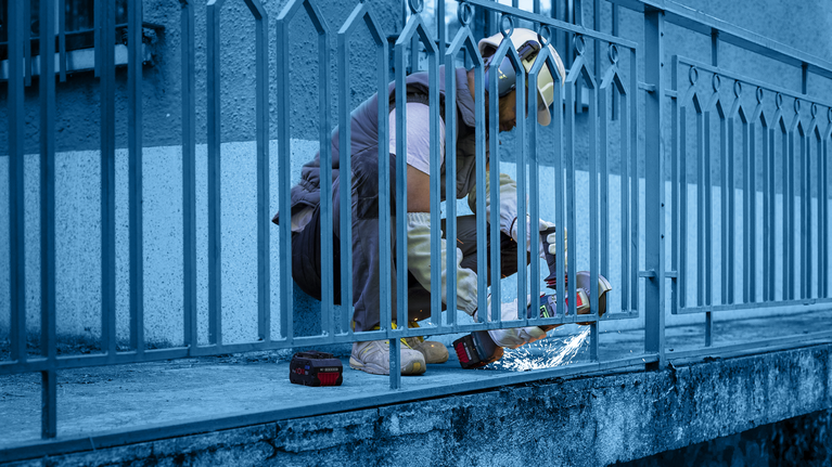 Person wearing safety equipment uses a power tool to cut a metal fence.
