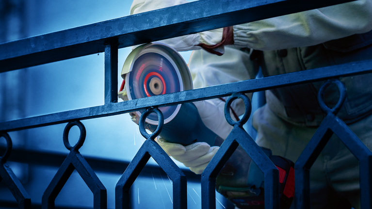 EXPERT Diamond Metal Wheel X-LOCK Cutting Disc 125 x 22.23 mm A person wearing safety equipment grinds a metal fence with a power tool.