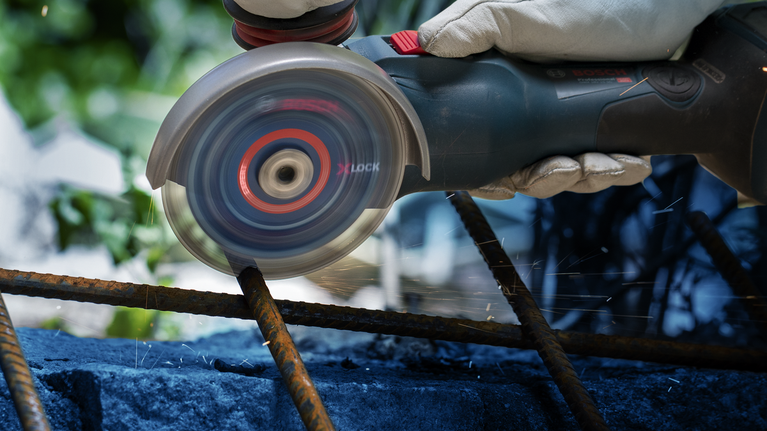 EXPERT Diamond Metal Wheel X-LOCK Cutting Disc 125 x 22.23 mm Person wearing safety equipment uses an angle grinder to cut through rusty rebar.
