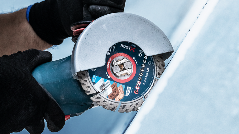 EXPERT MultiMaterial Diamond Cutting Disc 125 x 22.23 x 2.2 x 12 mm A person wearing safety equipment cuts a tile using an angle grinder.