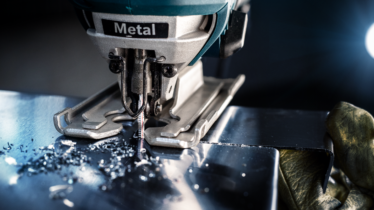 Person wearing safety equipment guides a jigsaw cutting through a metal sheet.