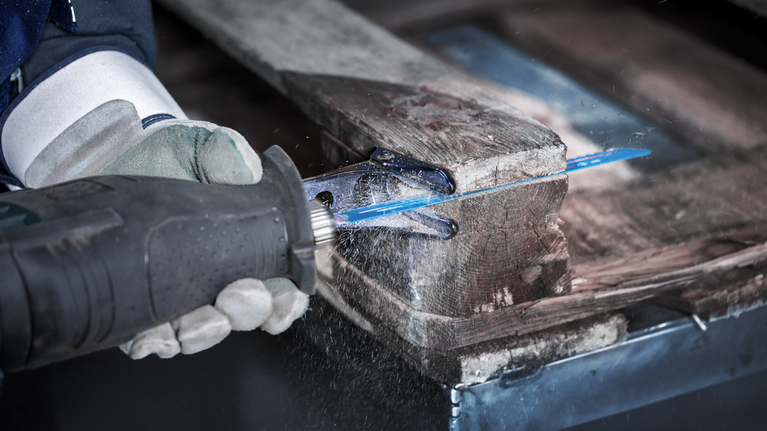 EXPERT Hard Nail Pallets S1122CHM Reciprocating Saw Blade 1-pc Person wearing safety equipment uses a reciprocating saw to cut through a wooden pallet.