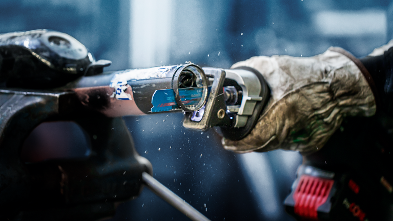 EXPERT ‘Medium-Thick Tough Metal’ S 955 HHM Reciprocating Saw Blade 1-pc Person wearing safety equipment uses a reciprocating saw to cut through a metal pipe.