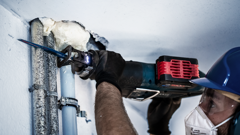 EXPERT ‘Multi Material’ 956 XHM Reciprocating Saw Blade 1-pc A person wearing safety equipment cuts through metal pipes using a reciprocating saw.