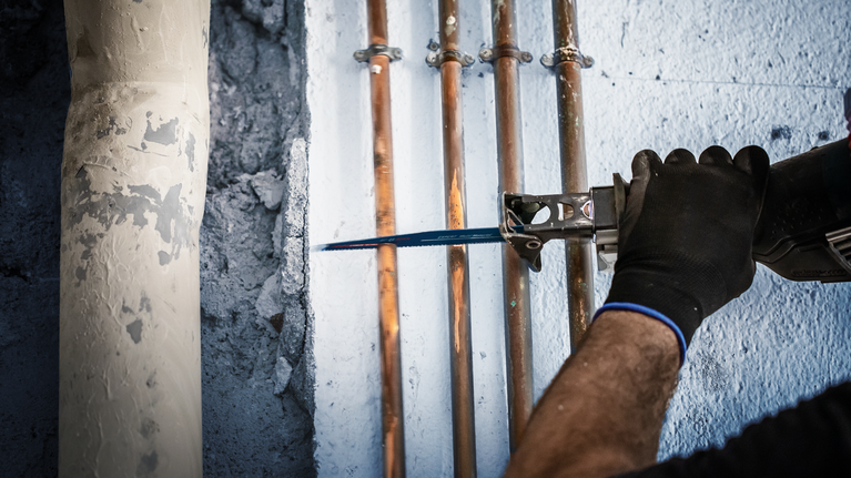 EXPERT ‘Multi Material’ 956 XHM Reciprocating Saw Blade 1-pc Person using a reciprocating saw to cut a copper pipe mounted on a wall.