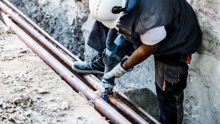 EXPERT ‘Thick Tough Metal’ S 555 CHC Reciprocating Saw Blade 1-pc Person wearing safety equipment uses a power tool to cut an old metal pipe outdoors.