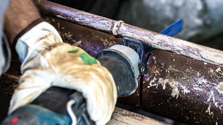 EXPERT ‘Thick Tough Metal’ S 555 CHC Reciprocating Saw Blade 1-pc A person wearing safety equipment cuts a rusted metal pipe with a reciprocating saw.