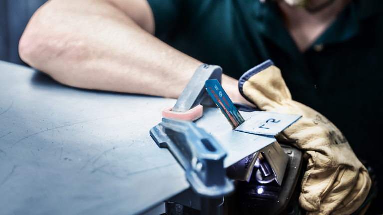 EXPERT ‘Thin Tough Metal’ S 522 EHM Reciprocating Saw Blade 1-pc Person wearing safety equipment holds metal sheet with gloved hand while using a jigsaw.