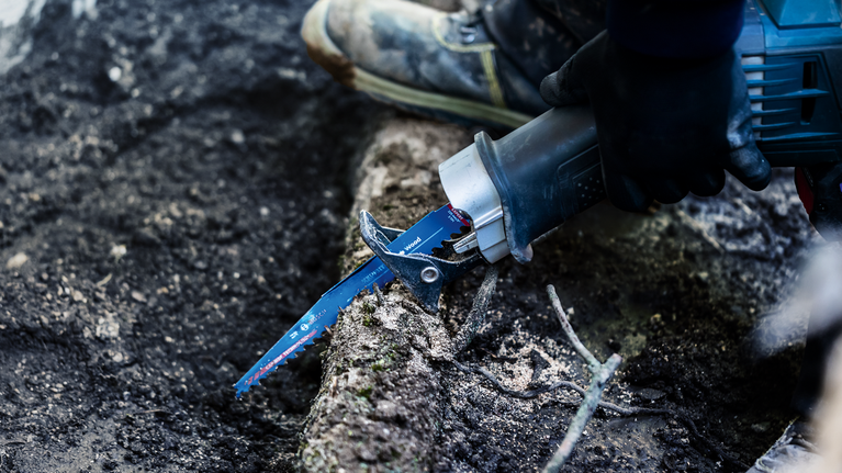 EXPERT ‘Tough Wood’ S 1142 KHM Reciprocating Saw Blade 1-pc Person wearing safety equipment uses a reciprocating saw to cut through a tree root.