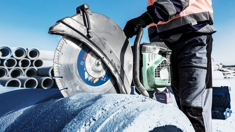 EXPERT MultiMaterial Diamond Cutting Disc 350 x 20/25.40 x 3.3 x 15 mm Person wearing safety equipment cuts a large concrete pipe with a power saw.
