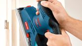 Person holds an electric sander to smooth a wooden door frame.