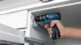 A person holds a compact cordless combi drill with a blue and black body.