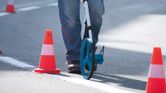 Person measuring road distance with a measuring wheel between traffic cones.