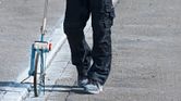 Person wearing safety equipment uses a measuring wheel to check distance on a paved road.