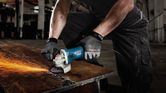 A person wearing safety equipment grinds metal, producing sparks on a workbench.