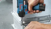 Person using a cordless impact wrench to fasten a bolt on a metal surface.