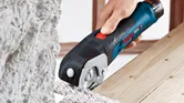 A person cuts soft building material using a cordless universal shear.