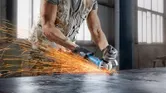 Person wearing safety equipment grinds metal, producing bright sparks.