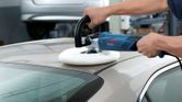 A person polishes a car roof with an electric polisher in a workshop.