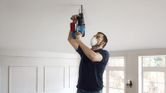 A person wearing safety equipment drills into a ceiling with a power tool.