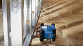 Laser leveling tool projecting guidelines beside metal wall frames on a construction floor.