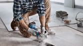 A person wearing safety equipment cuts a tile with a cordless power tool.