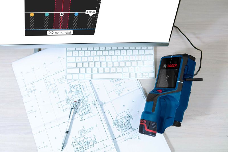 Digital wallscanner detector on architectural blueprints beside a computer keyboard.