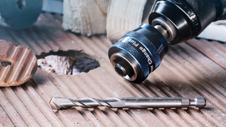 EXPERT Power Change Plus Pilot Drill Bit HSS-Co 7.15 x 105 mm Drill and bit placed on a grooved tile surface next to a freshly made hole.