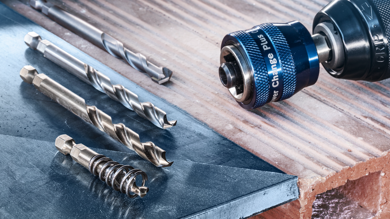 Drill driver with several drill bits placed on a metal and brick surface.