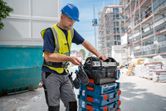 A person wearing safety equipment organizes toolboxes at a construction site.