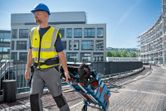 A person wearing safety equipment pulls a loaded tool cart and tool bag on a construction site.