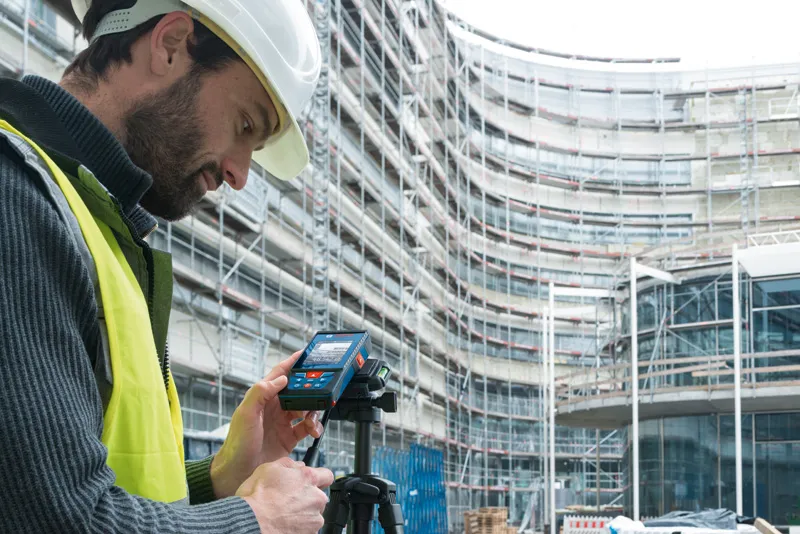 GLM 100-25 C A person wearing safety equipment operates a laser measure at a construction site.