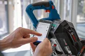Person adjusts cordless mitre saw settings using a smartphone app.